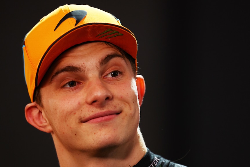 A headshot of Oscar Piastri, wearing an orange McLaren cap, staring on during an F1 night session.