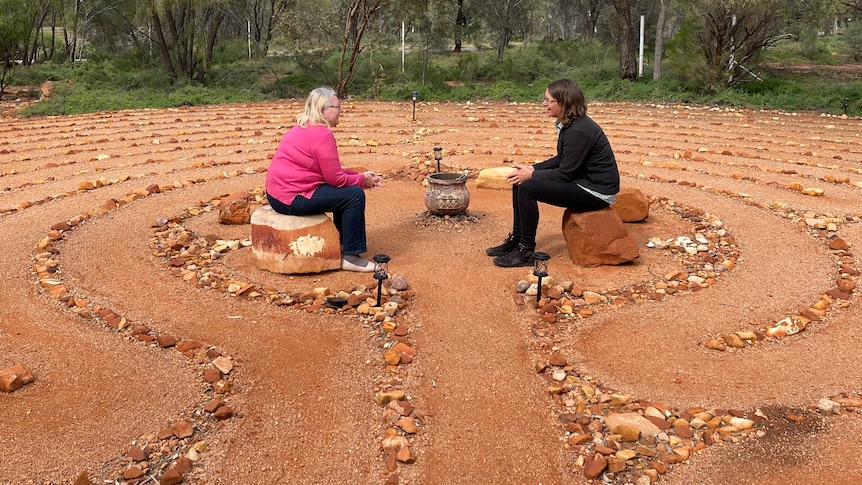Two smiling women sitting and chatting in the centre of a contemplative labyrinth