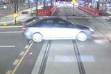 A car on the tracks in front of a light rail vehicle.