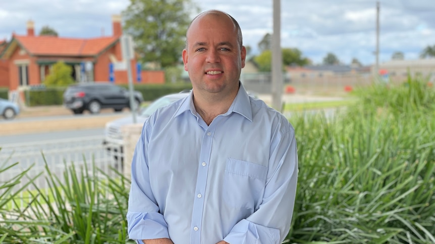 A man smiling at the camera with a garden in the background