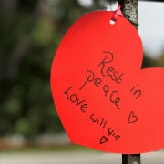 Red paper heart with rest in peace, love will win tied to iron fence.