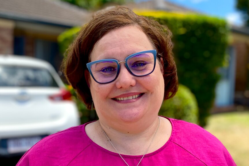 A woman in a pink top and glasses smiling.