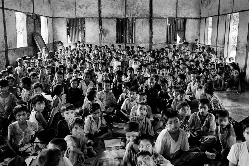 Scores of Rohingya children pack into a classroom and stare up at the camera.