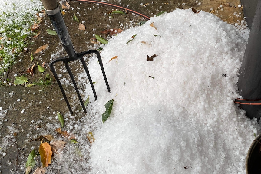 A pitchfork in a large mound of hail in a backyard.