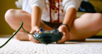 A girl sits with an x box control on the ground