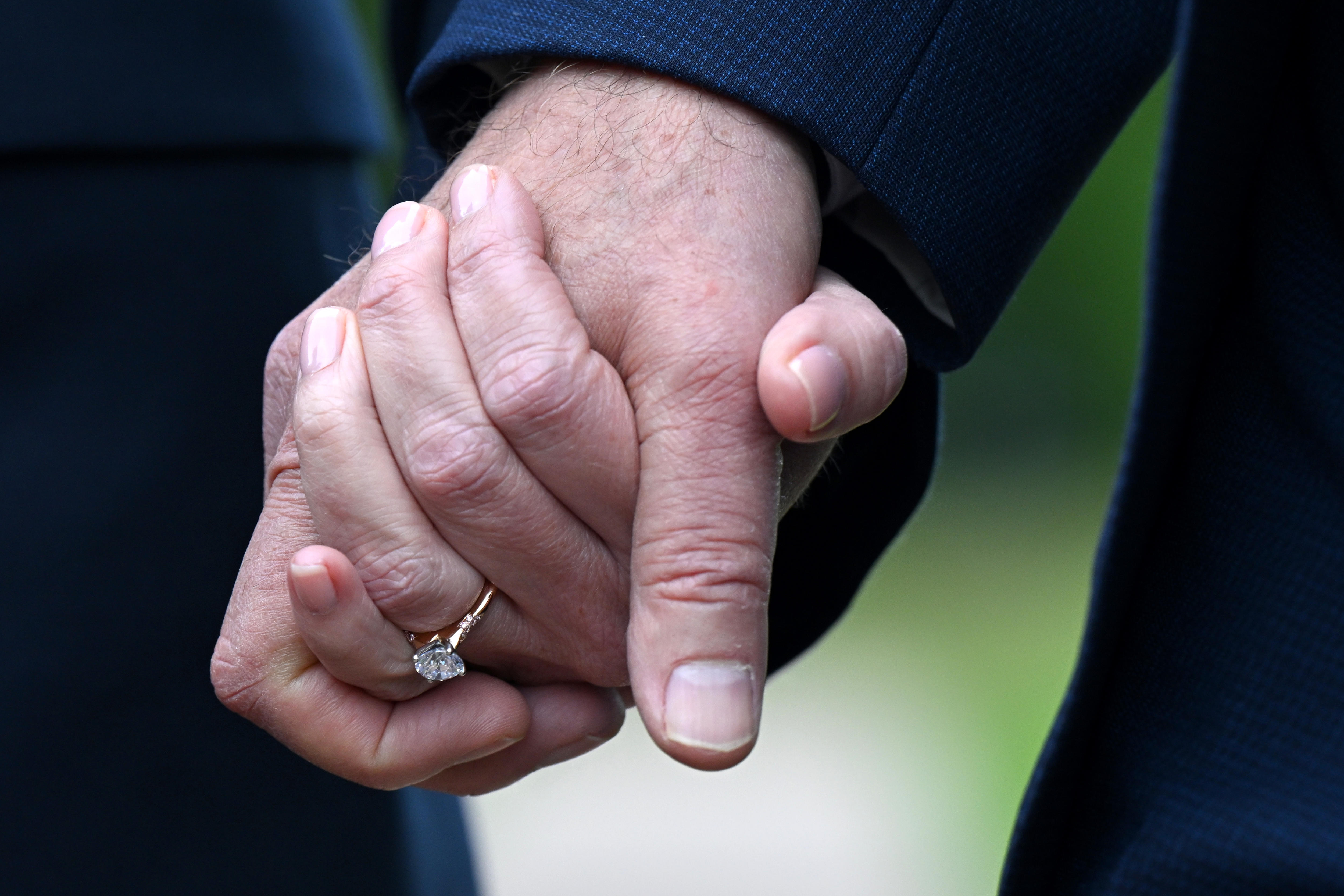 Un primer plano de las manos entrelazadas de un hombre y una mujer. La mujer lleva un anillo de diamantes en el dedo anular. 