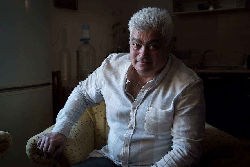 A man sits in an armchair and looks at the camera as he poses for a photograph