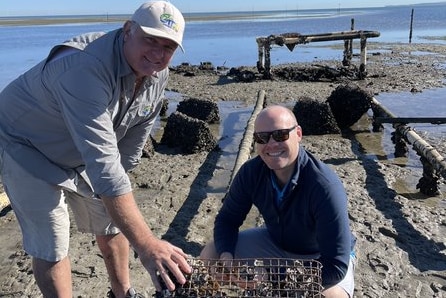 Photo of two men crouching in front of oyster shells