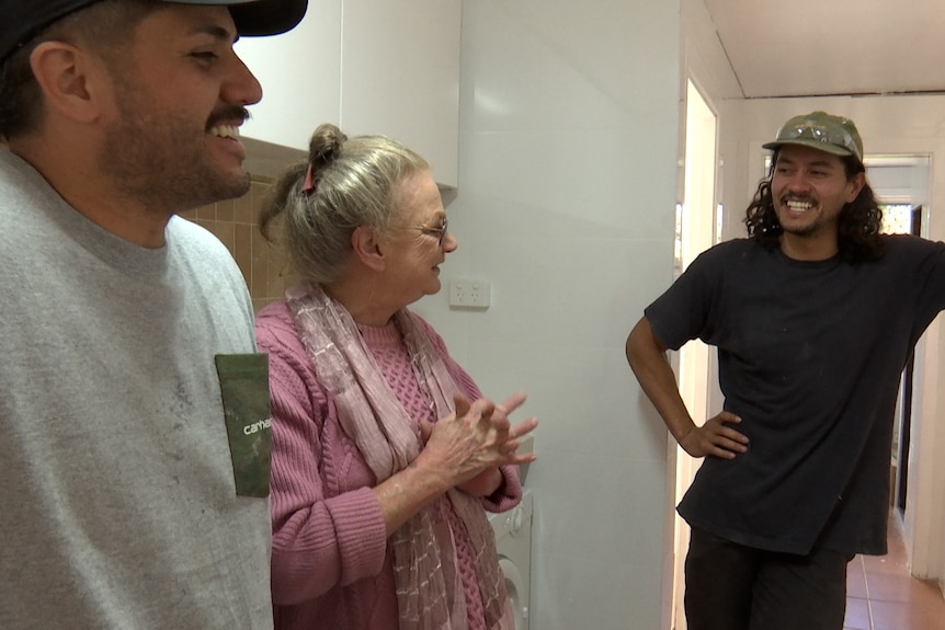 An older woman standing in between two younger men inside a home