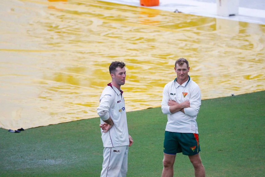 Jimmy Peirson and George Bailey speak while standing in front of wet pitch covers.