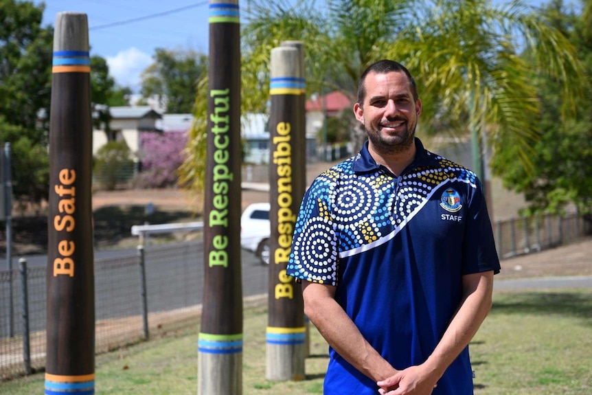 A man stands in front of totem poles reading be safe, be respectful, be responsible outside Eidsvold State School.