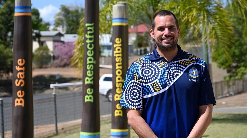 A man stands in front of totem poles reading be safe, be respectful, be responsible outside Eidsvold State School.