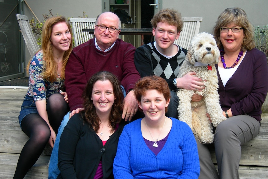 A family of two adults and four children posing for the camera with their dog