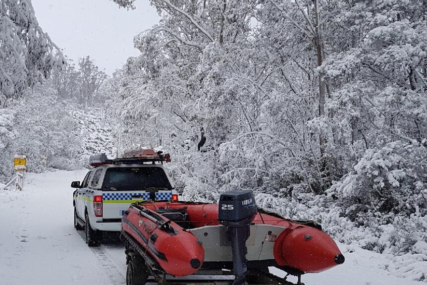 Police car towing boat in snow.