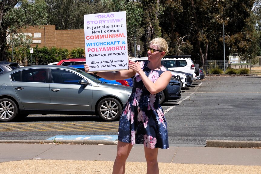 A woman holds up a sign in protest against a drag queen event.