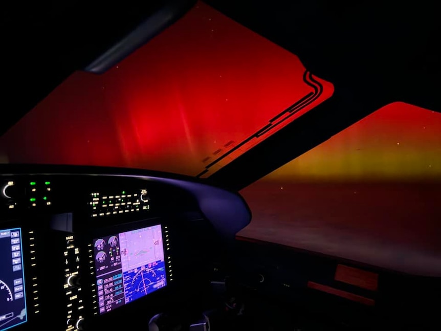 A small plane's cockpit dashboard with bright red and yellow hues in the distance outside the window.