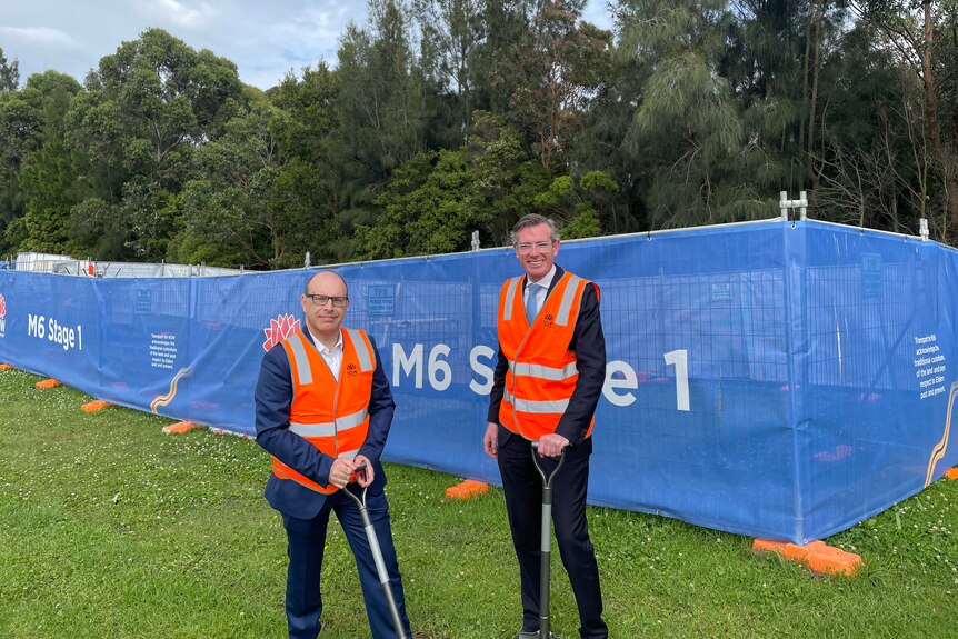 Two men stand together in hi-vis vests and shovels at a sod turning event