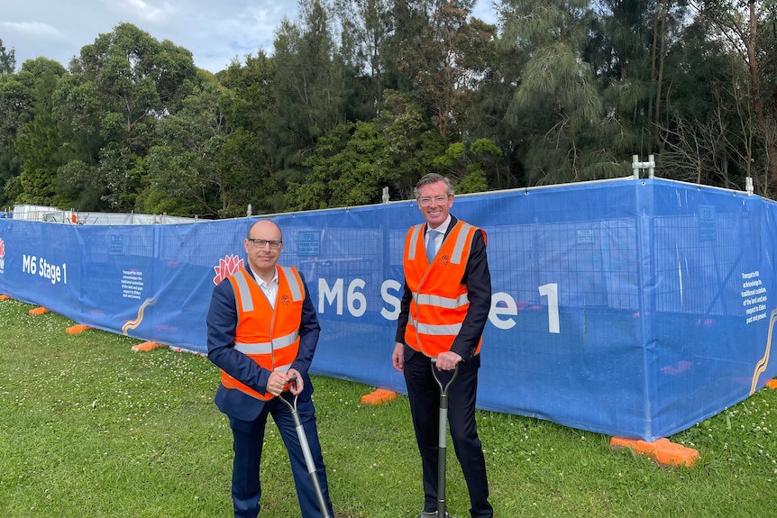 Two men stand together in hi-vis vests and shovels at a sod turning event