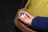 A woman holds an Airtag in her hand near her bag.