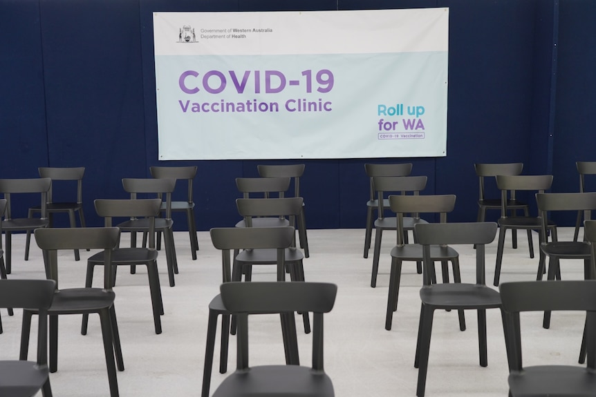 Rows of empty black chairs with a COVID-19 vaccination clinic sign on the wall behind.