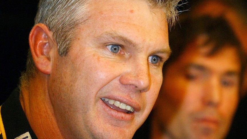 Danny Frawley, wearing a black and yellow Richmond shirt, speaks at a press conference.