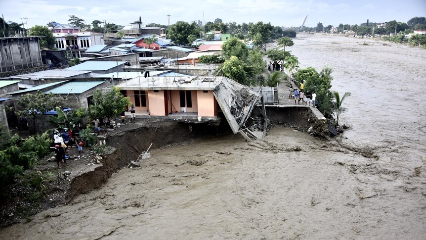 An aerial shot shows murky floodwaters eroding land and undermining houses and other structures.