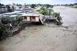 An aerial shot shows murky floodwaters eroding land and undermining houses and other structures.