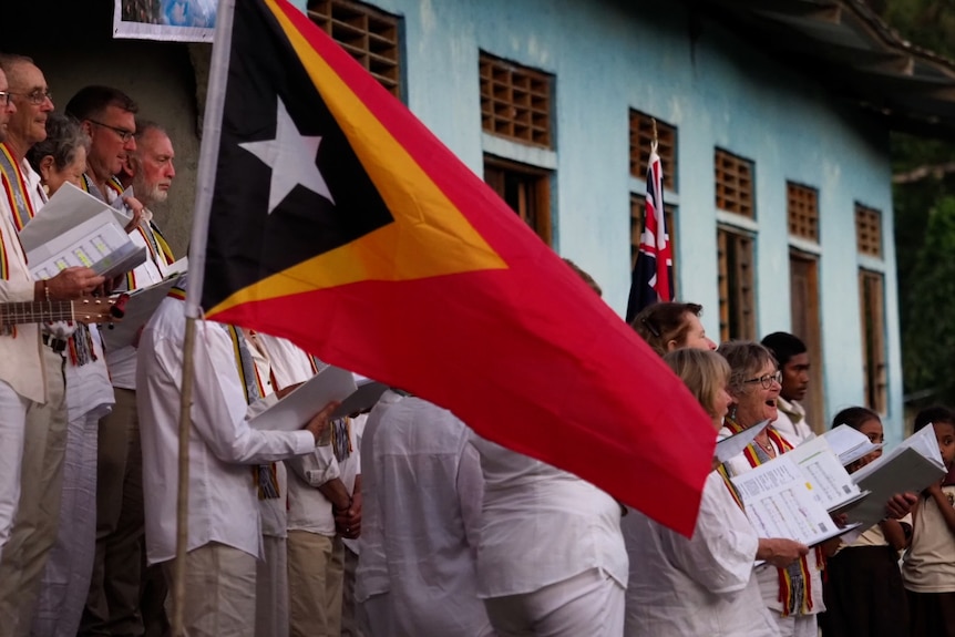 Australian choir performing with East-Timor building in background and East Timor flag in foreground
