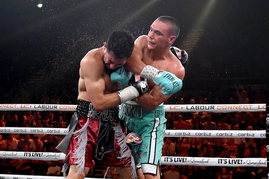 Two male boxers together in the ring, one with their head down, grimacing, the other having just punched him.