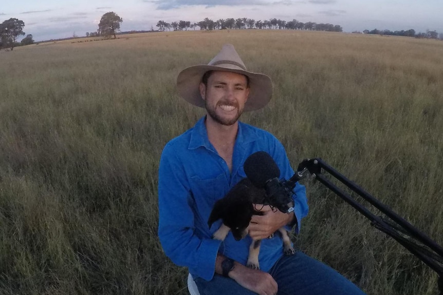 A man with a puppy sits in a field preparing a podcast.