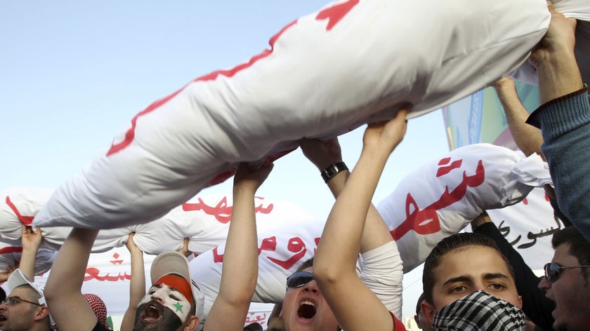 Syrians carry the "bodies" of those who died in recent protests as they shout slogans during a protest.