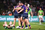 A group of NRL players huddle around a teammate who has just scored a try as an opposition player lies on the ground.