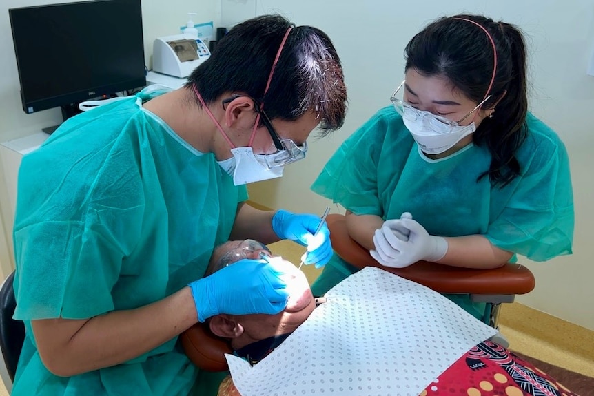 Two student dentists examine the mouth of a male patient.