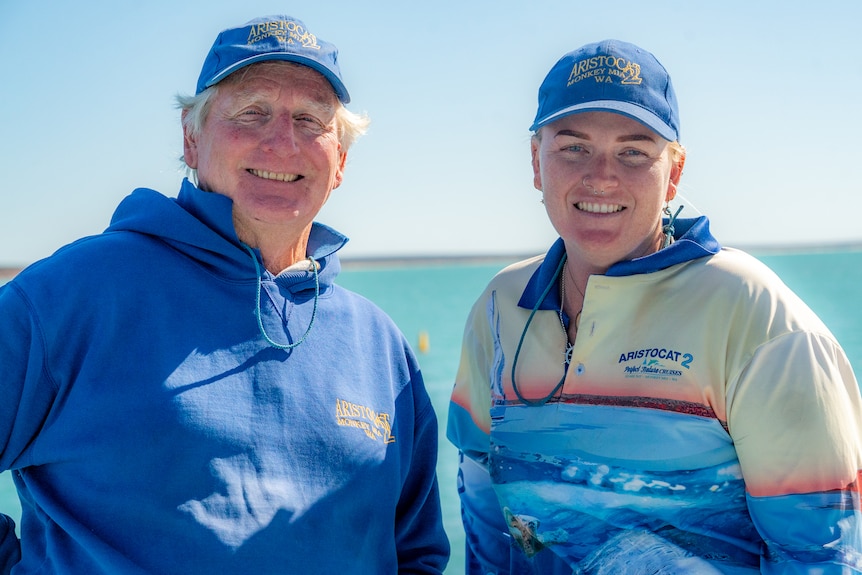 Un homme et une femme debout sur un bateau, portant des casquettes, avec l'océan en arrière-plan à Shark Bay. 