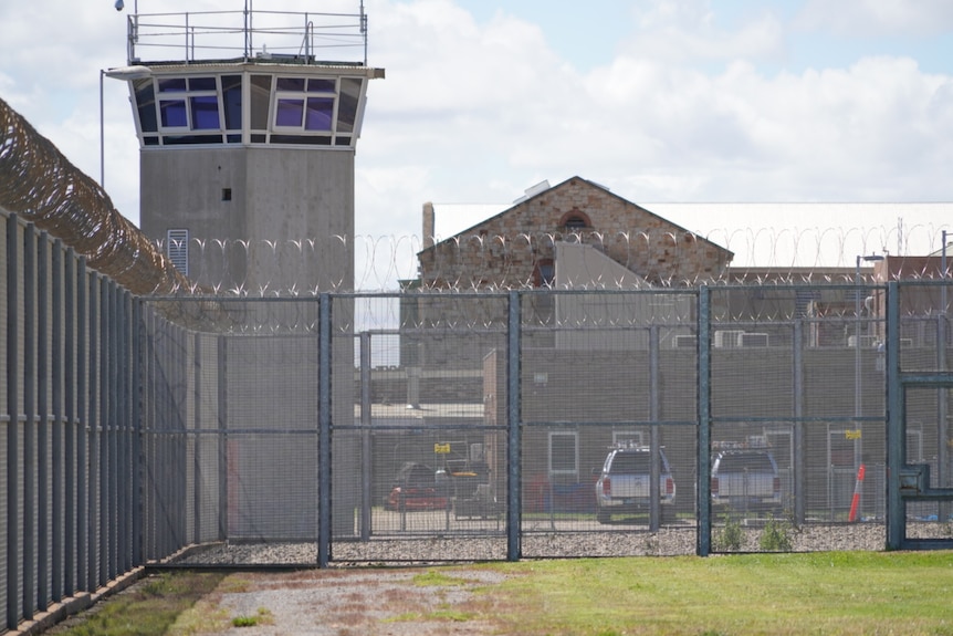 A prison fence in front of a watch tower and building