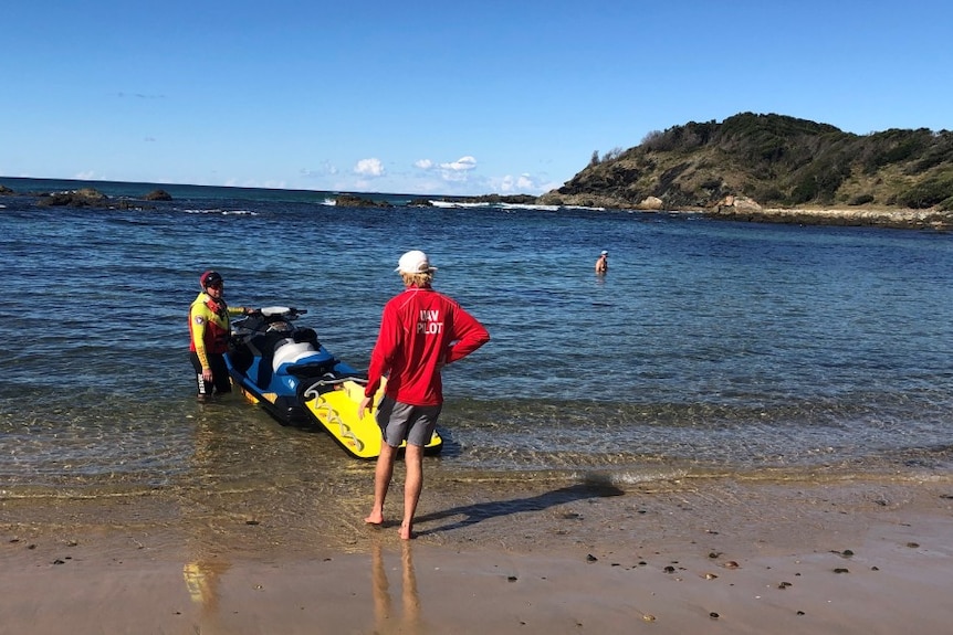 A man beside a jetski in the water at a beach.