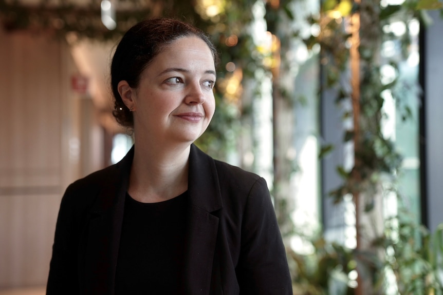 Davina Rooney looks to her left, with plants hanging behind her.