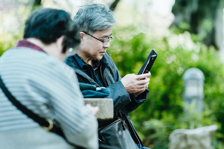 An older man uses a mobile in a flip case in a park