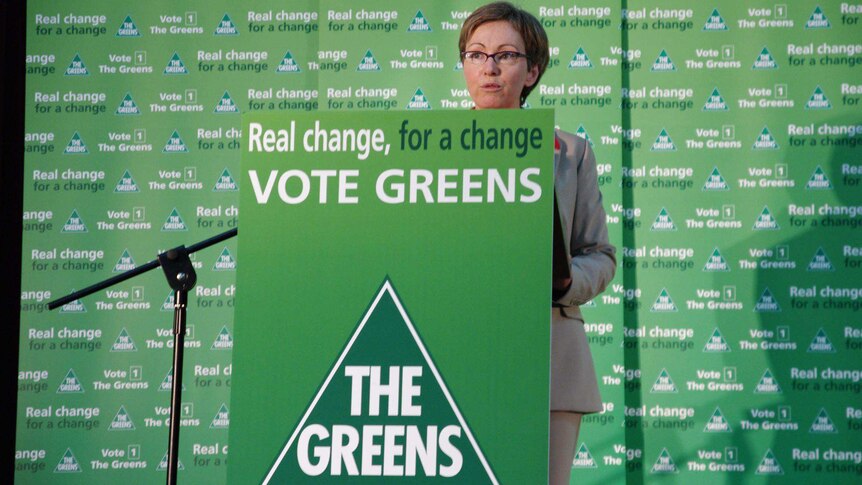 Woman giving a speech in front of Greens signage.