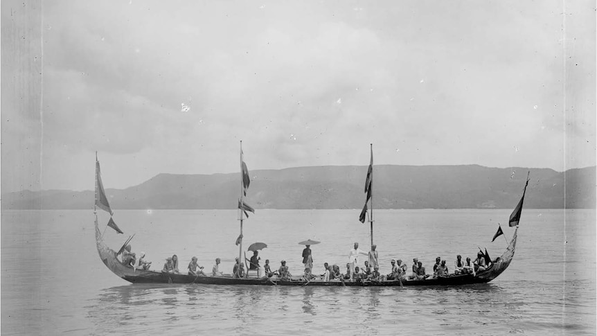 A black and white image of a number of people sitting and standing on a long boat in the ocean