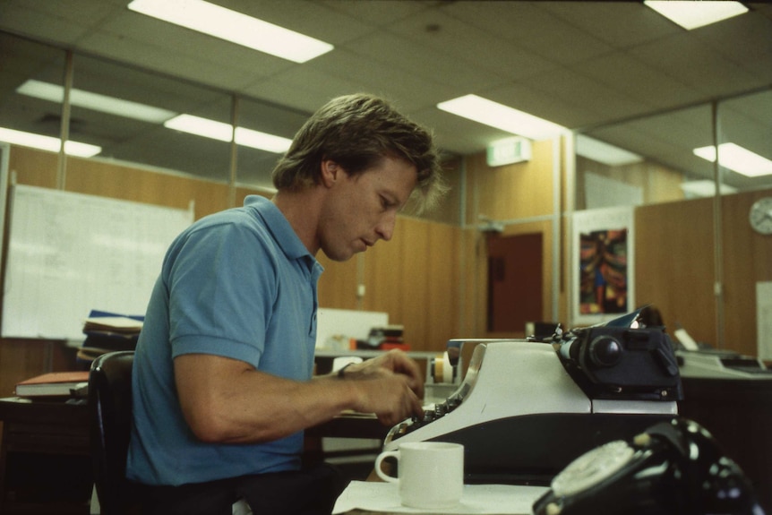 An AM reporter sits at a typewriter in a newsroom.