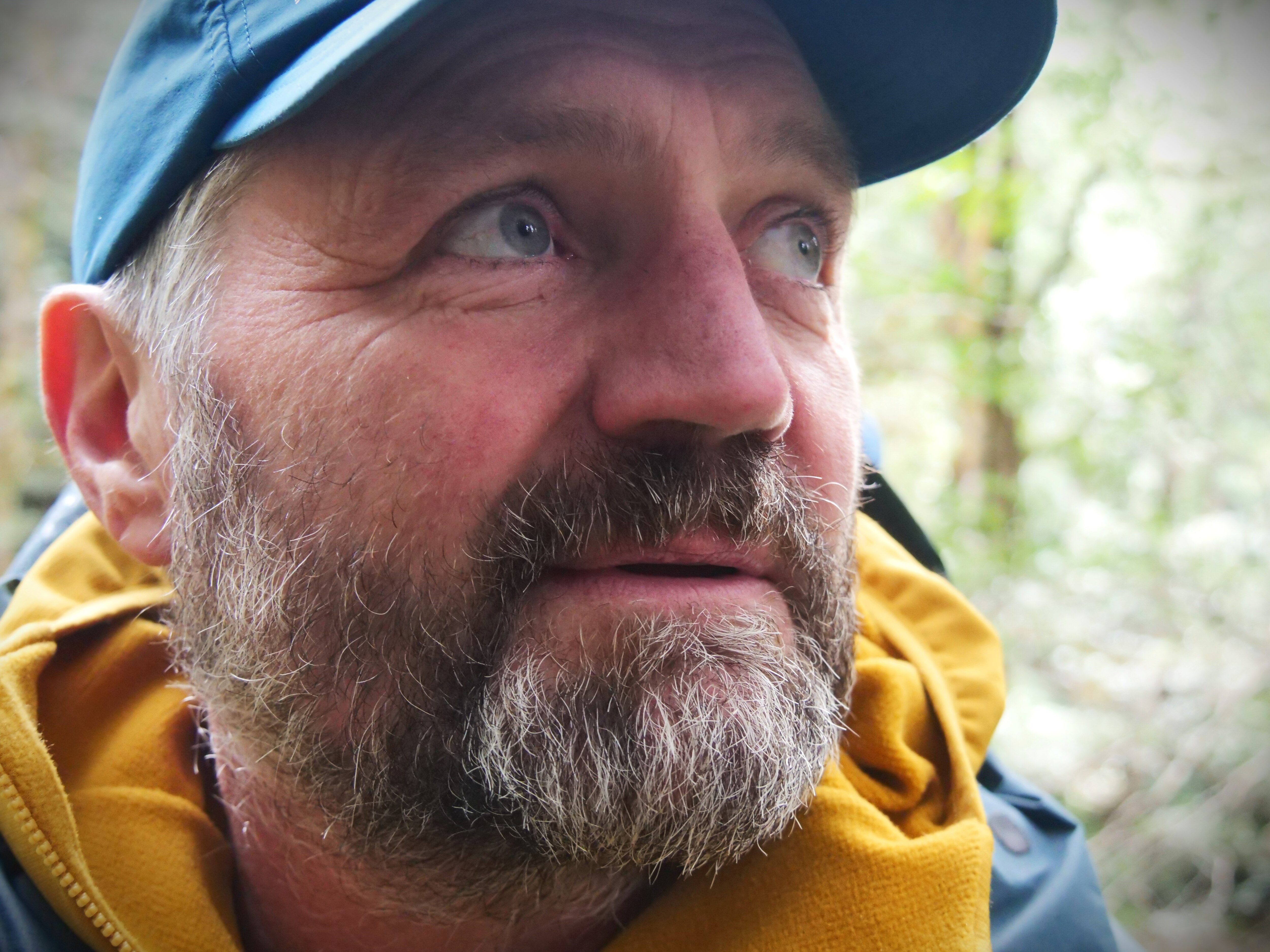 A close up photograph of an unshaven man with blue eyes looking off into the distance.