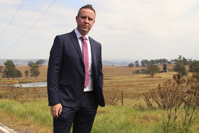 A man in a suit stands on a rural road.