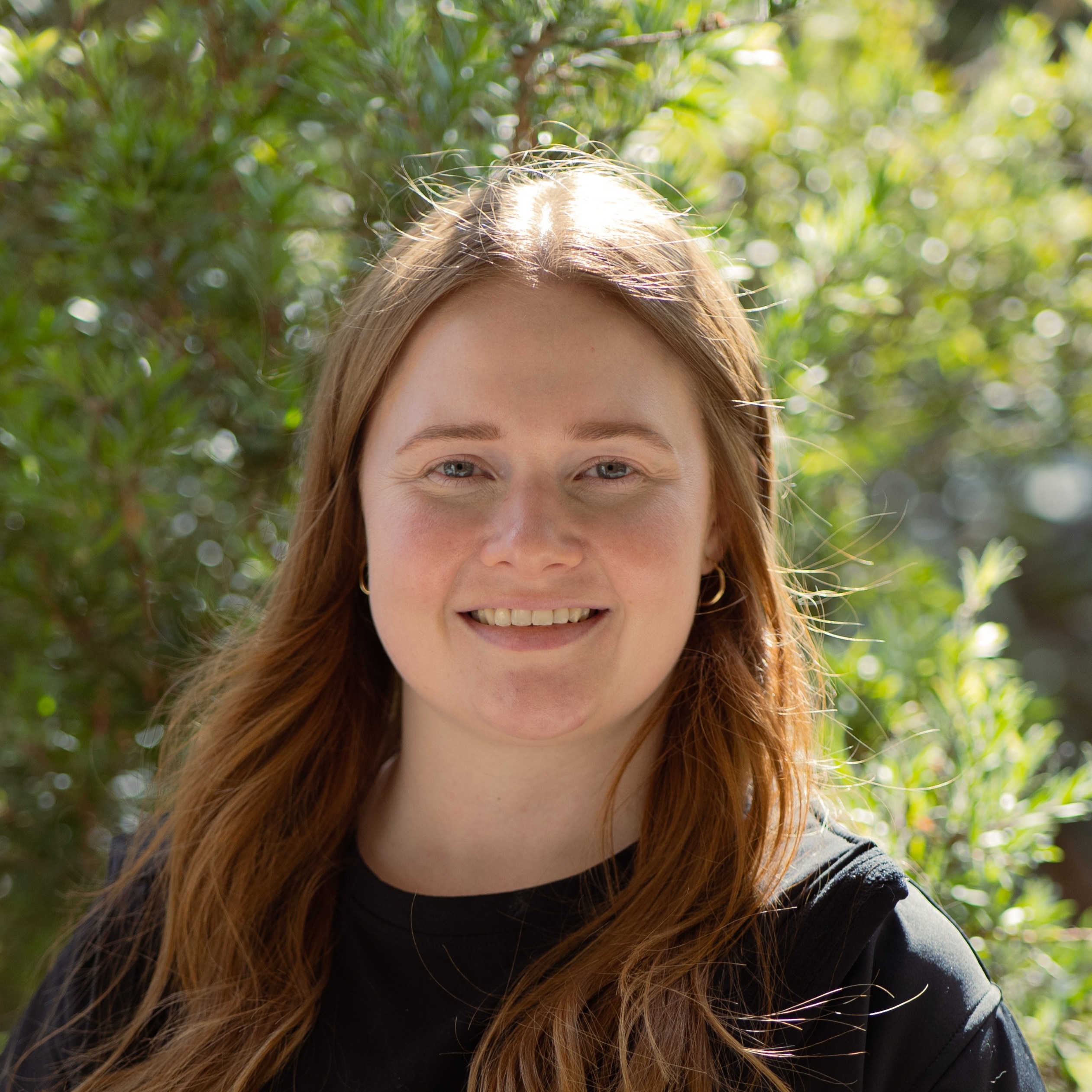 Jade Currie, a young woman, smiles in outdoor headshot 