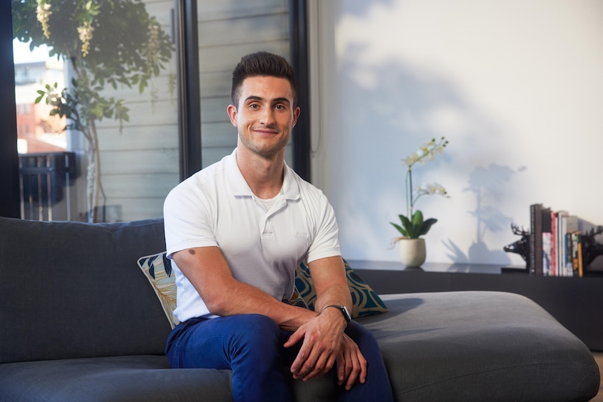 Alex Rodriguez a brown haired man wearing a white polo shirt and blue pants sitting on a couch. 