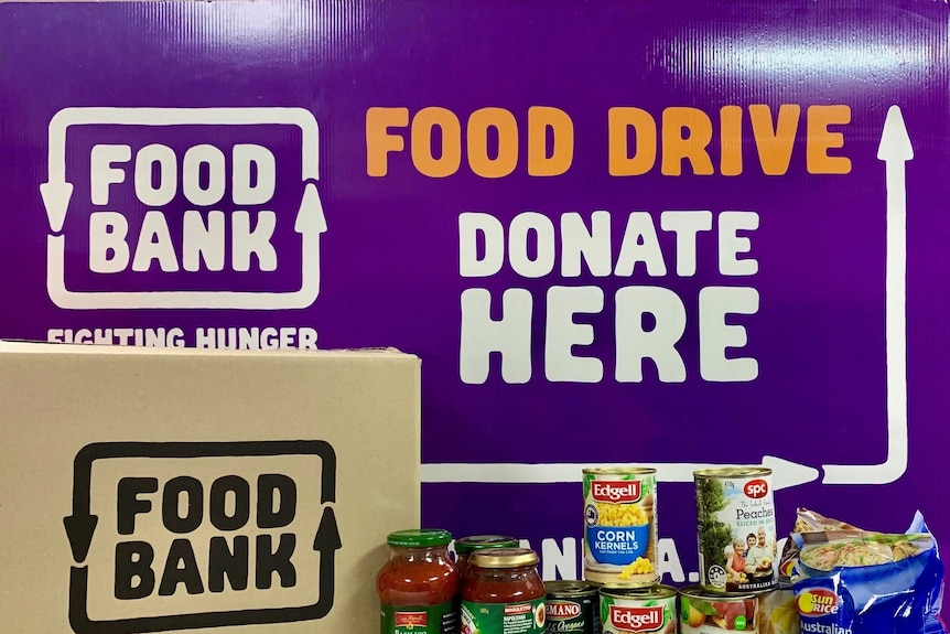 Donated tins and jars of food in front of a Foodbank box and sign.