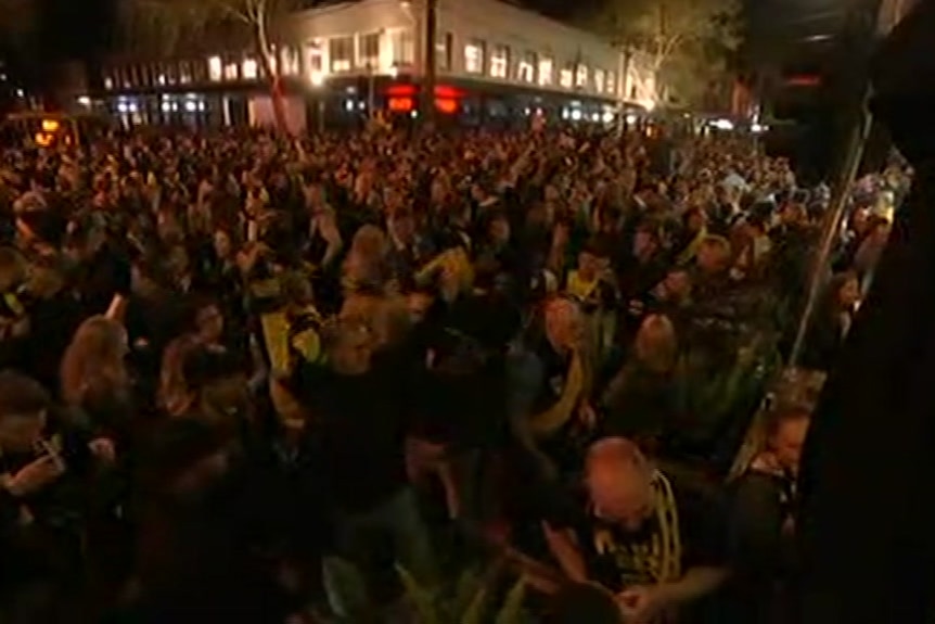 A huge crowd at an intersection at Swan Street in Richmond, many wearing yellow and black scarves.