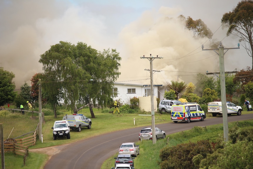 Police and ambulance outside a house with smoke billowing from the roof.