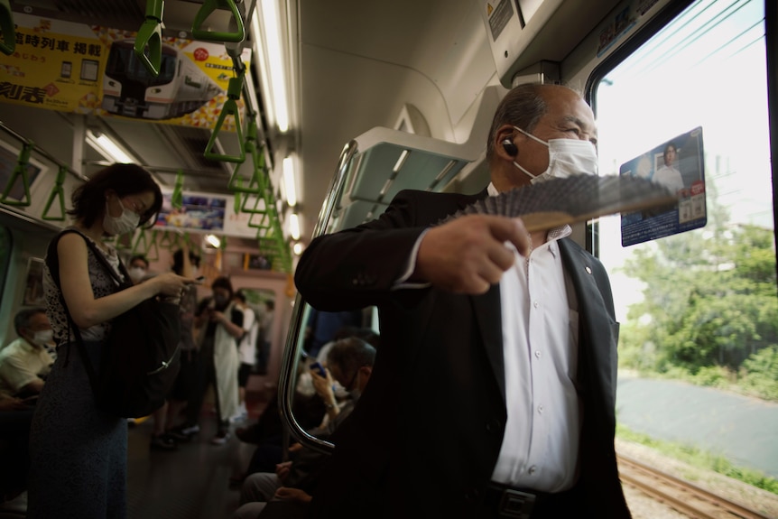 Mężczyzna korzysta ze składanego wentylatora podczas jazdy pociągiem w Tokio