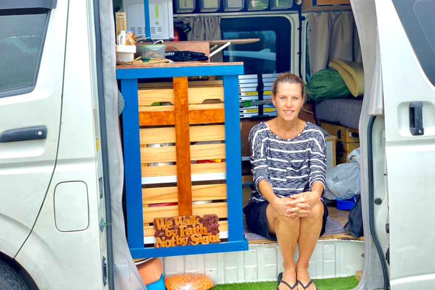 Woman sitting in sliding doorway of a van beside inbuilt cupboards.